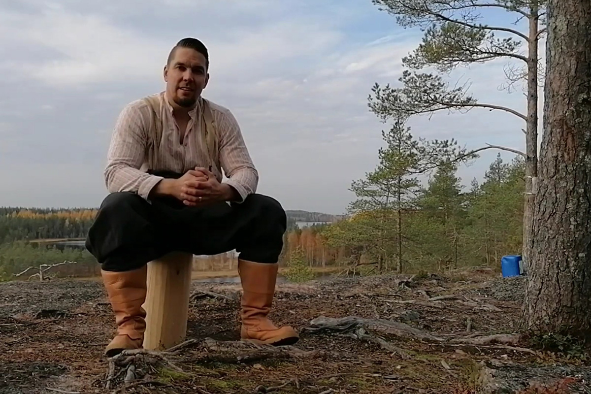 "Marko Pehkonen istuu metsässä, taustalla kaunis luontomaisema."